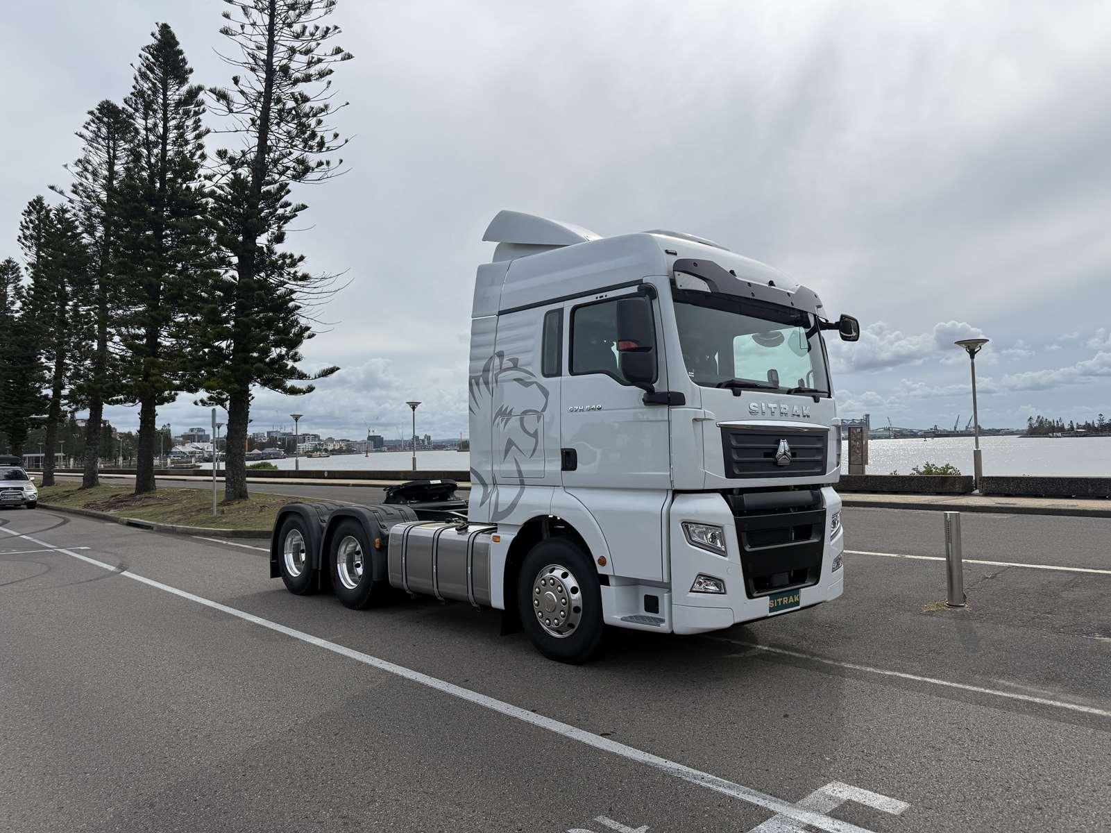 White Sitrak prime mover parked by a waterfront with trees